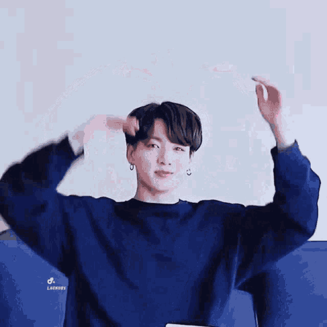 a man in a blue sweater is making a heart shape with his hands .