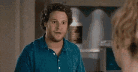 a man in a blue shirt is talking to a woman in a room and says `` back the fuck '' .