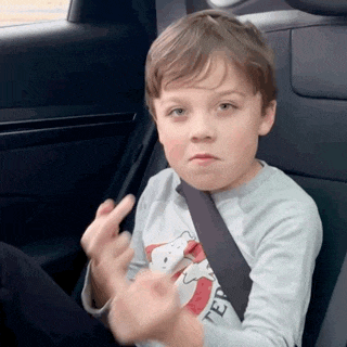 a young boy is sitting in the back seat of a car making a face .