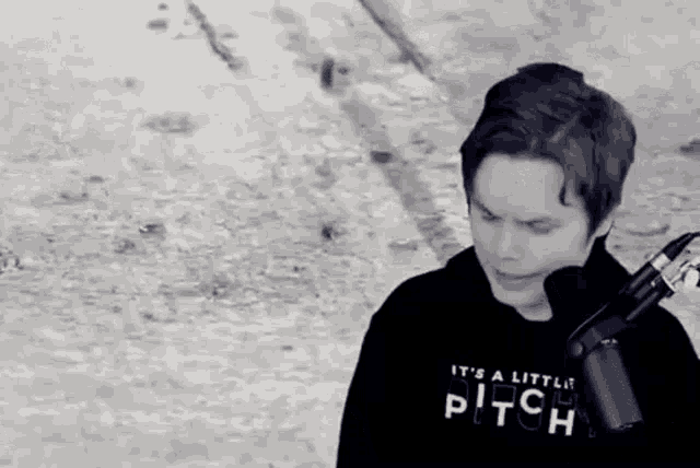 a young man is standing in front of a microphone wearing a hoodie that says it 's a little pitch .