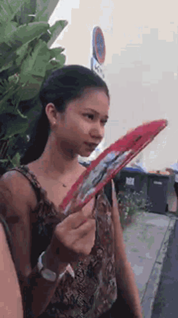 a woman is holding a red fan in her hand and looking at it .