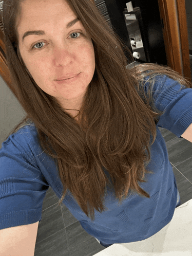 a woman in a blue shirt takes a selfie in a bathroom