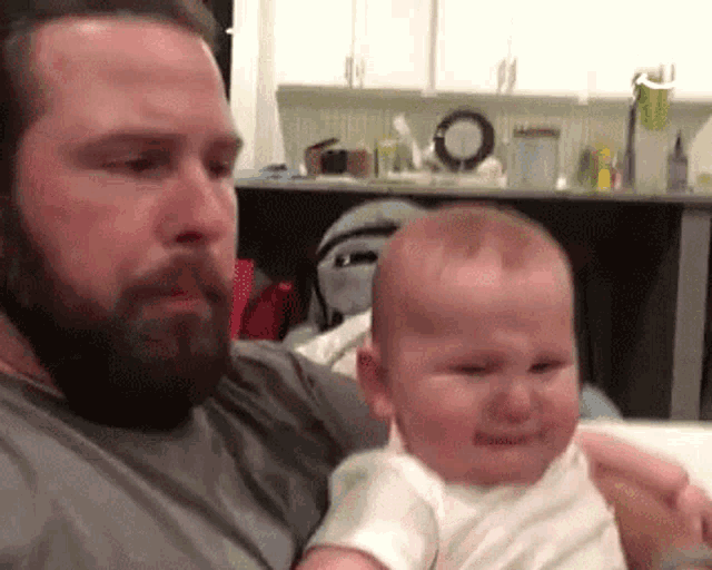 a man is holding a crying baby in his arms in a kitchen .