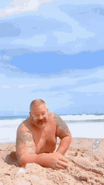 a shirtless man laying in the sand on a beach