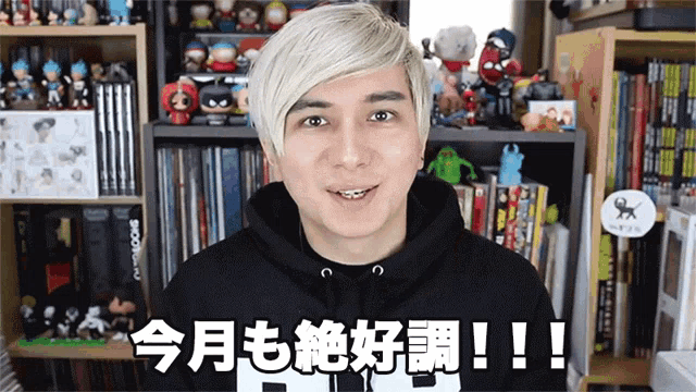 a man wearing a black hoodie is standing in front of a bookshelf with foreign characters on it