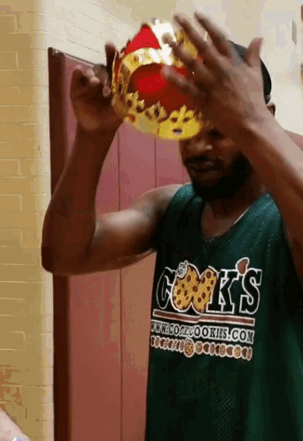 a man wearing a cook 's shirt holds a crown over his head
