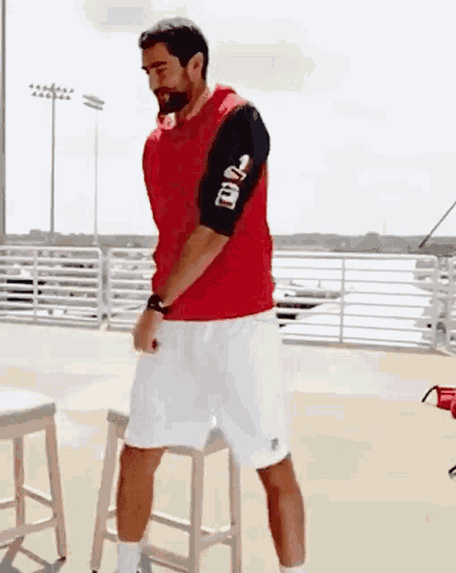 a man in a red vest and white shorts is standing on a stool with the number 2 on his arm