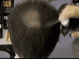 a person is spraying a bottle of glue on a man 's hair .
