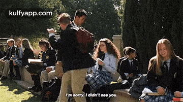a group of people in school uniforms are sitting on a bench and a man is standing next to a girl .