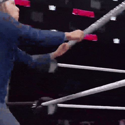 a man in a blue shirt is standing in a wrestling ring with a microphone in his hand