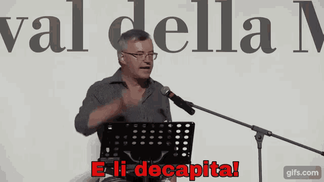 a man stands in front of a microphone with the words e-li decapita in red letters