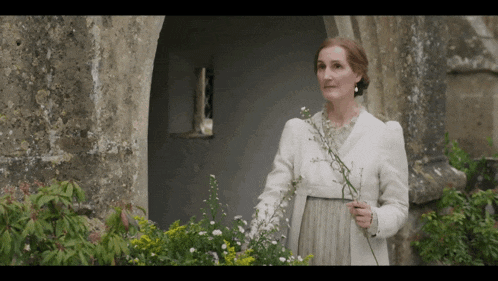 a woman in a white coat holds flowers in her hand