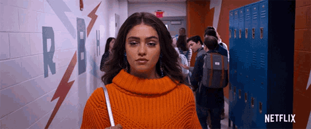 a girl in an orange sweater stands in a hallway with lockers and a netflix logo