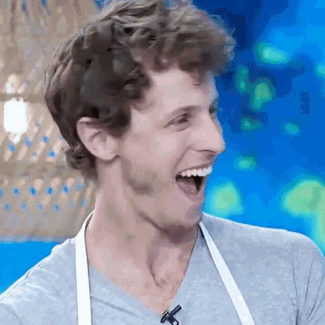a man wearing an apron and a grey shirt is laughing with his mouth open