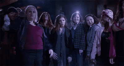 a group of women are standing next to each other in a dark room and looking at something .