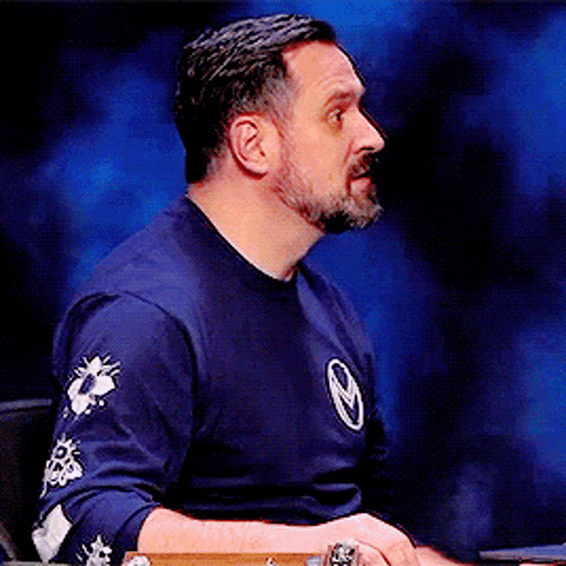 a man with a beard is wearing a blue shirt with a circle on the sleeves