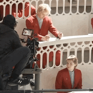 a man in a red jacket sits at a table while a woman in a red jacket looks on
