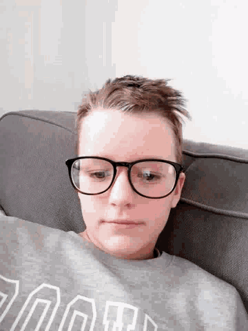 a young man wearing glasses and a grey sweatshirt with the word hood on it is laying on a couch
