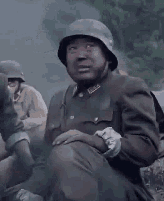 a soldier wearing a helmet is kneeling down with his mouth open in a field .