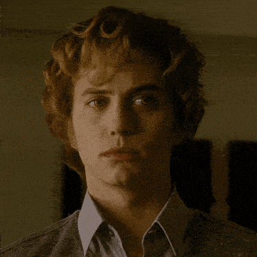 a close up of a man 's face with curly hair and a blue shirt