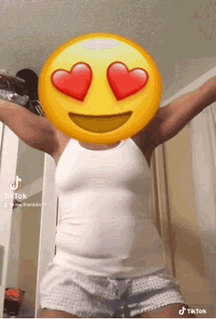 a woman wearing a white tank top and shorts has a smiley face on her face with hearts in her eyes .