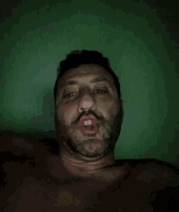 a shirtless man with a beard looks at the camera with his eyes closed