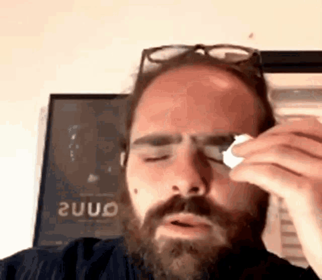 a man with a beard and glasses wipes his eye with a napkin