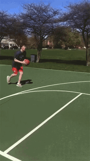 a man in red shorts is playing basketball on a green court