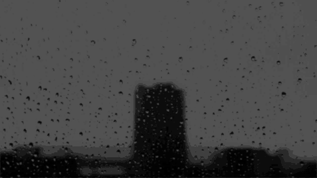 a black and white photo of rain drops on a window with a city skyline in the background