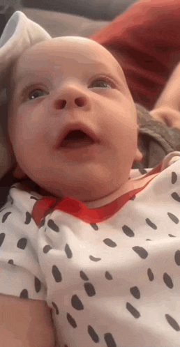 a baby wearing a dalmatian shirt is laying on a couch with his mouth open .