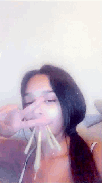 a woman is making a peace sign with her hands in front of her face while eating noodles .