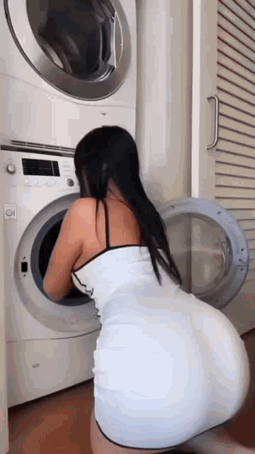 a woman in a white dress is kneeling in front of a washer and dryer .