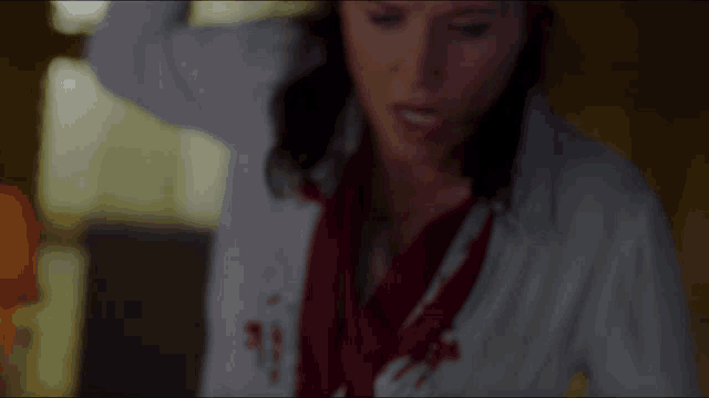 a woman in a white coat and red shirt is making a funny face while holding something in her hand .