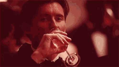 a man in a tuxedo is drinking a glass of red liquid .