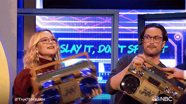 a man and a woman are holding boomboxes in front of a sign that says slay it , do n't sf