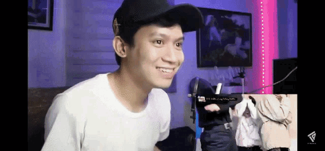 a man wearing a black hat and a white shirt is smiling while sitting in a living room .