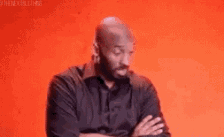 a bald man with a beard is standing with his arms crossed against a red background .