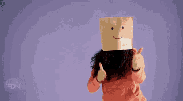 a woman with a cardboard box on her head giving a thumbs up sign