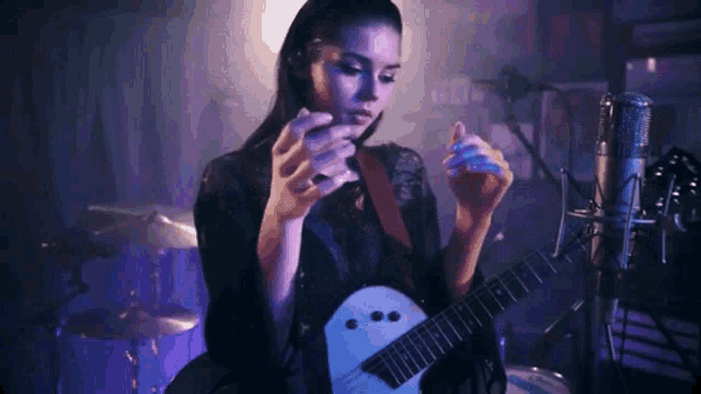 a woman is playing a guitar in front of a microphone and a drum set .