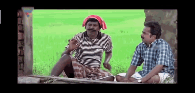 two men are sitting next to each other in a field talking .