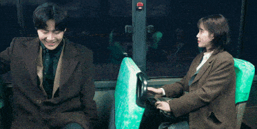 a man and a woman sitting on a bus with a green seat