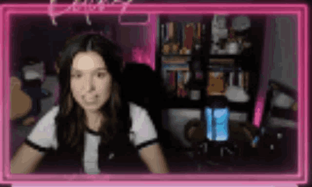 a girl is sitting in front of a computer screen with a pink neon frame .