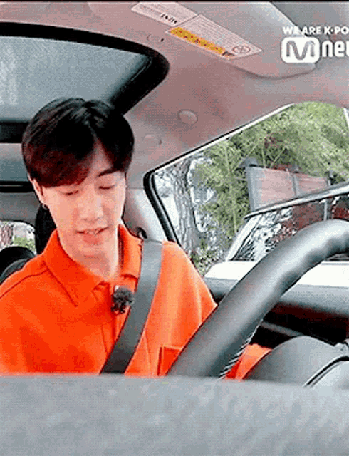 a man in an orange shirt is sitting in a car .