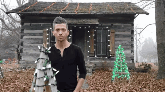 a man holding a christmas tree in front of a cabin