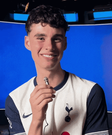a young man wearing a tottenham shirt is holding a microphone