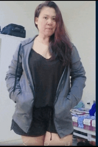 a woman wearing a grey jacket and black shorts stands in front of a bed