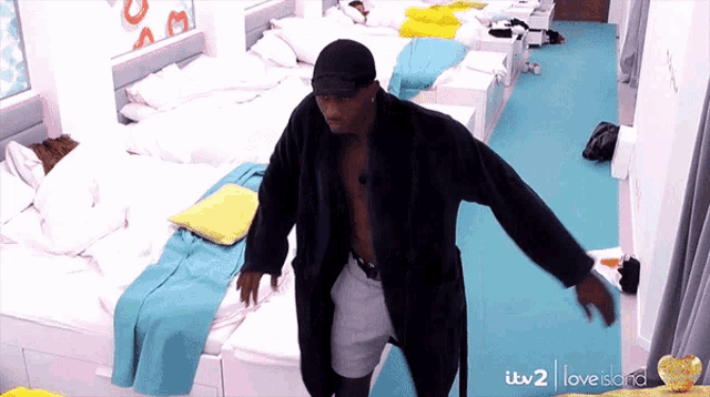 a man in a bathrobe is dancing in a room with lots of beds and a sign that says love island