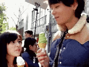 a man in a blue jacket is holding an ice cream cone next to a girl