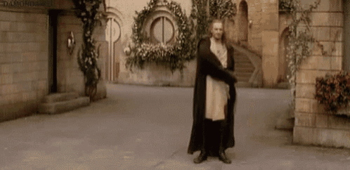 a man in a robe is standing in front of a building with flowers .