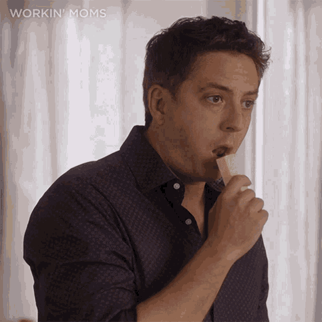 a man in a purple shirt is eating a piece of cheese with the words workin moms below him
